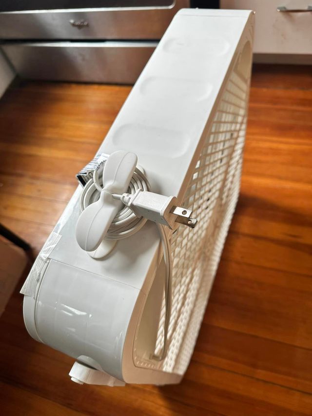 A white box fan with a white silicone cable organizer adhered to the side and the power cable coiled around it.