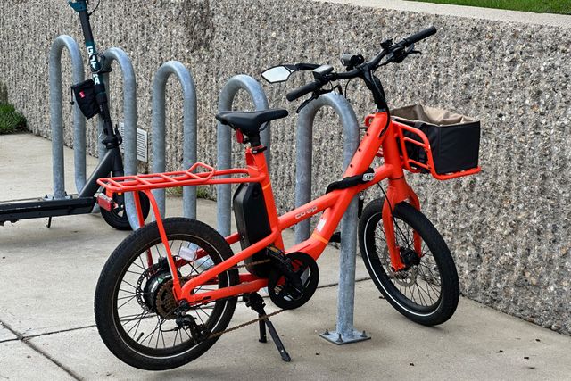 An orange bike against a speckled concrete wall. The speckling on the wall behind the bike is pronounced.