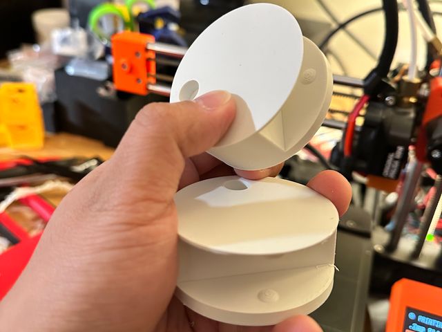 Two white cylindrical plastic objects with a slot through their middle and a divot on one side.