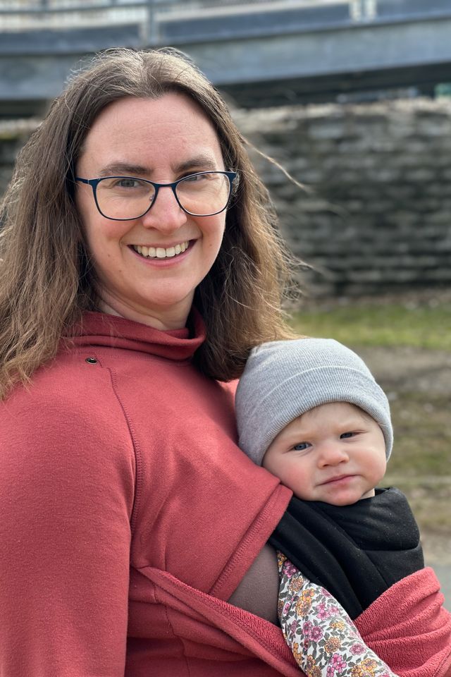 A smiling brown-haired woman with a baby strapped to her chest. The image is crisper, but there are some blurring artifacts around the edges of the woman's hair.