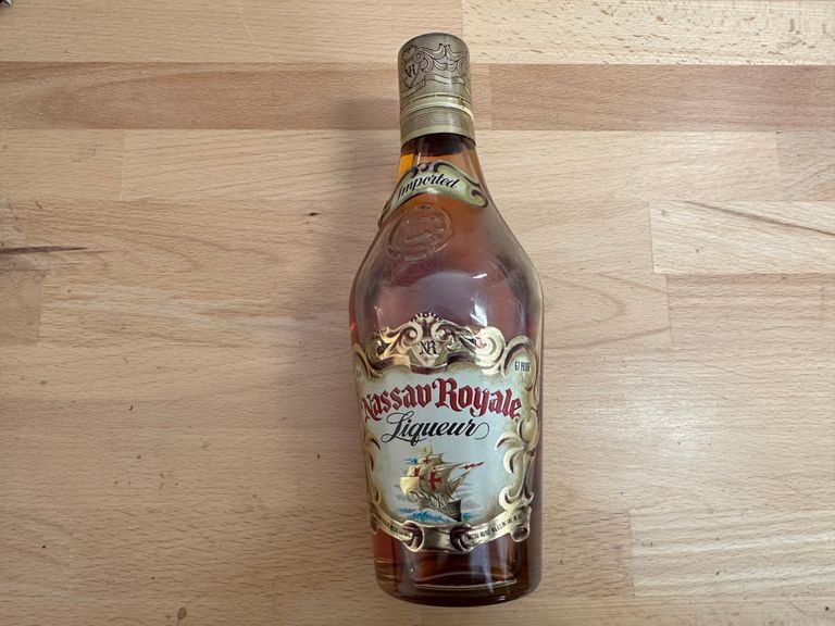 A dusty looking bottle of Nassau Royale on a wooden table.