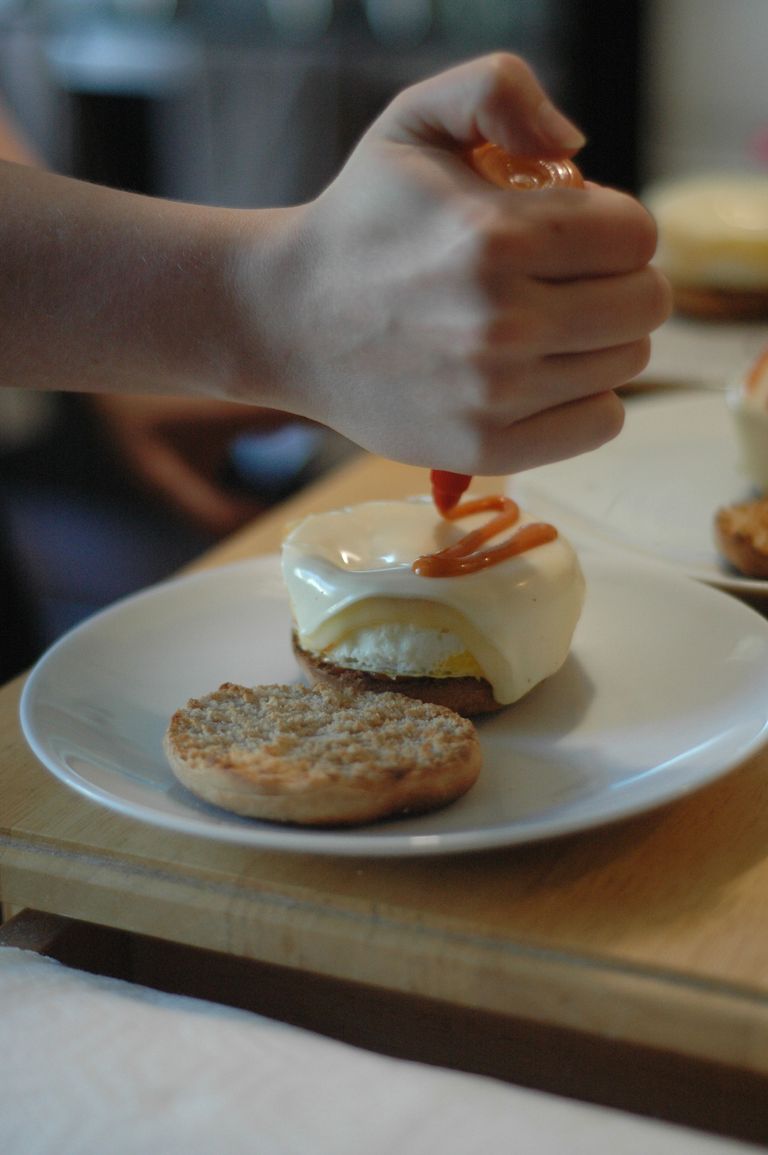 Close up of the breakfast sandwich receiving a drizzle of red hot sauce.