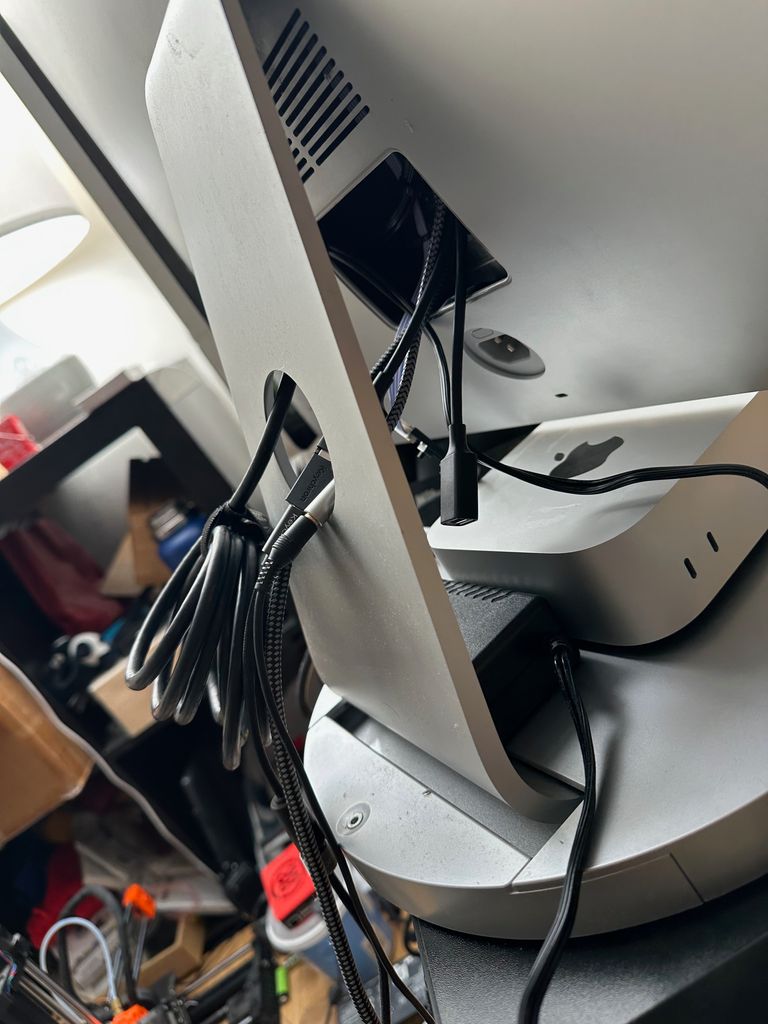 The back of the iMac, still showing a mess of cables protruding from a rectangular hole. They're slightly tidied with cable holders.