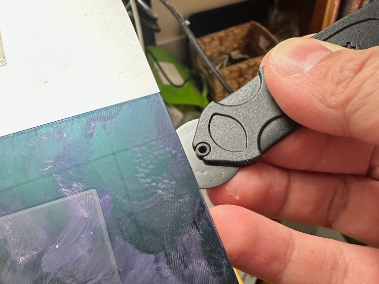 The edge of a glass iMac screen with a black tool resembling a plastic pizza cutter being run along the edge between glass and aluminum.