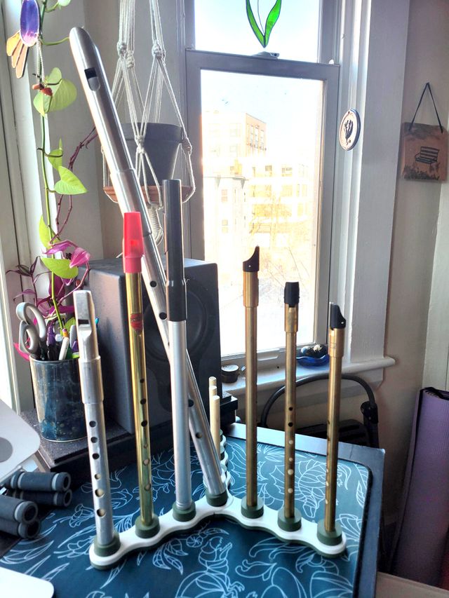 The whistle stand on a desk, loaded with whistles, but the large whistle in the center is leaning to the left, the connector at its base having come dislodged